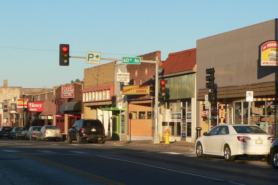 Row of storefronts along Maple Street with traffic signals and parked cars in the late-afternoon sun.