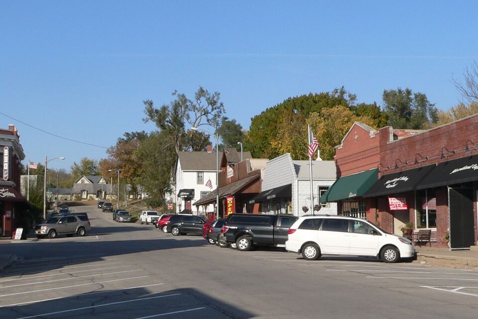 Main street in downtown Elkhorn lined with small brick storefronts, trees and parked cars.