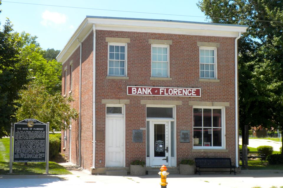 Two-story red brick building with a 'Bank of Florence' sign, a historical marker beside it, and trees around it.