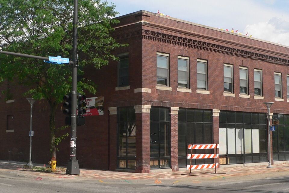 Two-story red brick commercial building on a street corner with trees along the sidewalk.