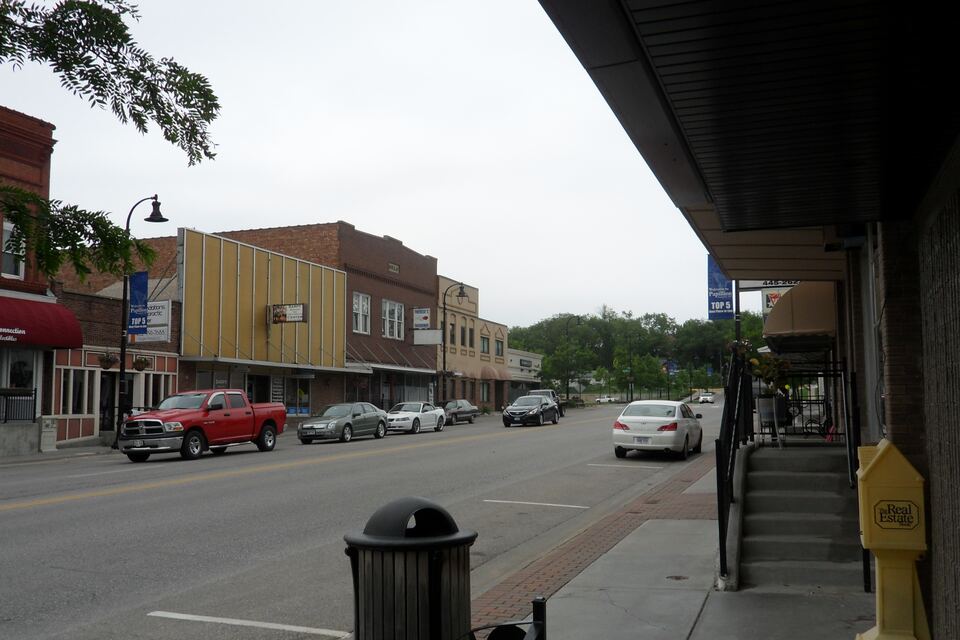 Washington Avenue in downtown Papillion with brick storefronts, a covered sidewalk and parked cars.