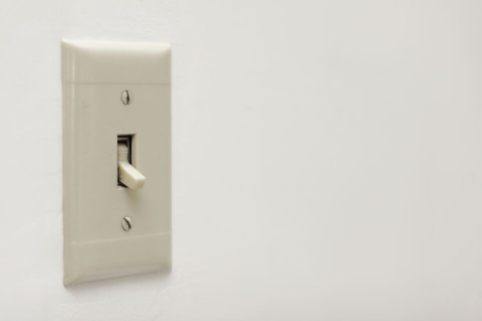 Close-up of an off-white toggle light switch and cover plate on a plain light-colored wall.